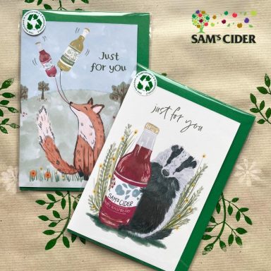 Two greeting cards featuring a fox and a badger, each holding a drink, on a patterned background.