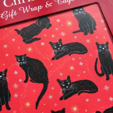 Red gift wrap featuring various illustrated black cats and snowflakes.