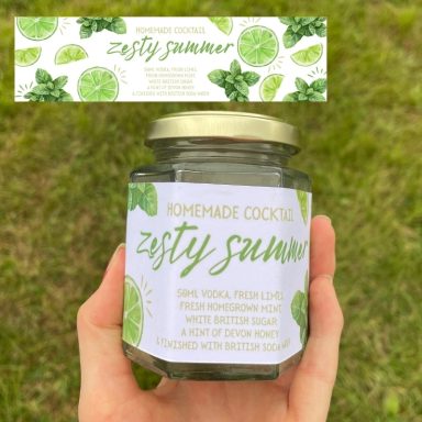 A hand holding a jar of homemade cookies labelled "Zesty Summer" with lime and mint decorations.
