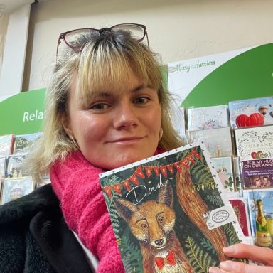 Person holding a greeting card featuring a fox design in a shop setting.