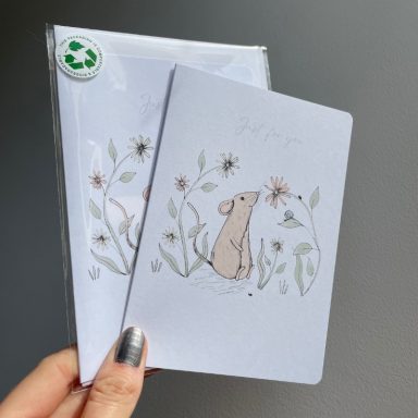 A hand holding two greeting cards featuring a mouse among floral illustrations.