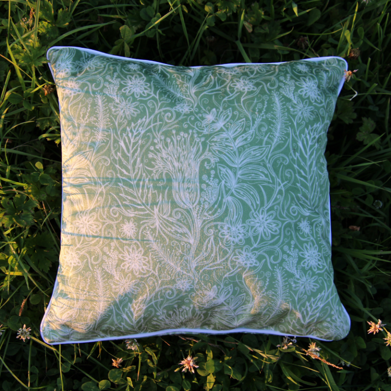 Green decorative cushion with a subtle floral pattern, placed on grass.