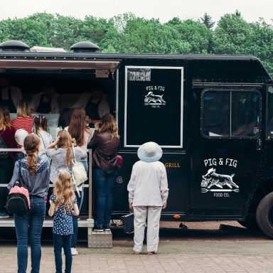 Crowd gathered around a black food truck with people at a park.