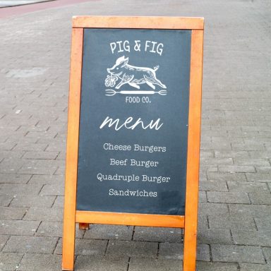 Outdoor menu board for "Pig & Fig" featuring burger options.