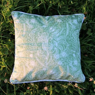 Green decorative cushion with a floral pattern, placed on grass.
