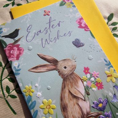 A decorative Easter card featuring a rabbit surrounded by flowers and a yellow envelope.